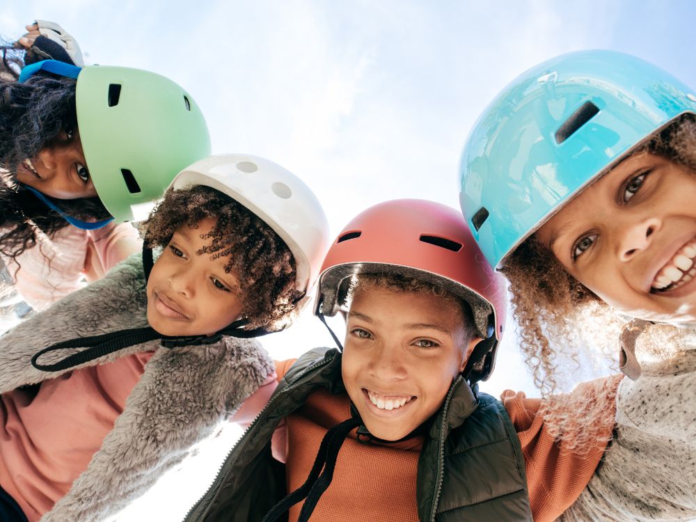 Crianças abraçadas em círculo usando capacete. Bicicletas, skates e patins são ótimos presentes para meninos e para meninas, só não esqueça o equipamento de segurança.