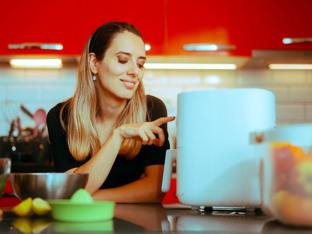 Mulher em sua cozinha utilizando uma air fryer branca. As melhores air fryer do mercado tornam a sua vida mais prática e saudável